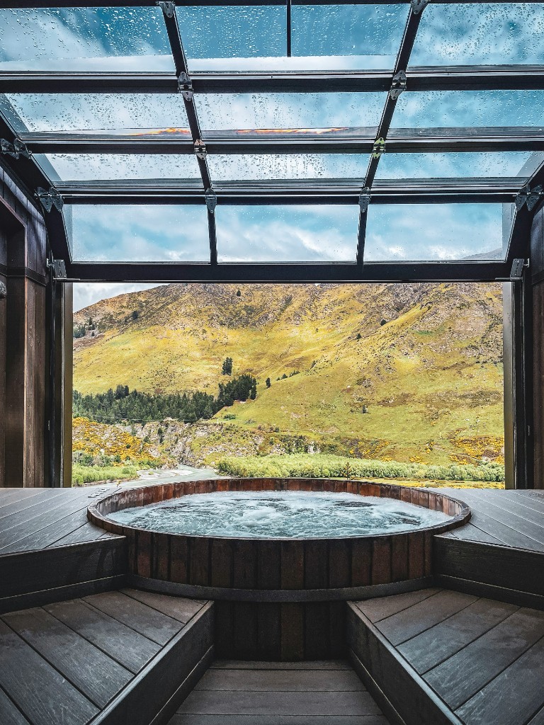 Wooden hot tub overlooking a green mountain hillside